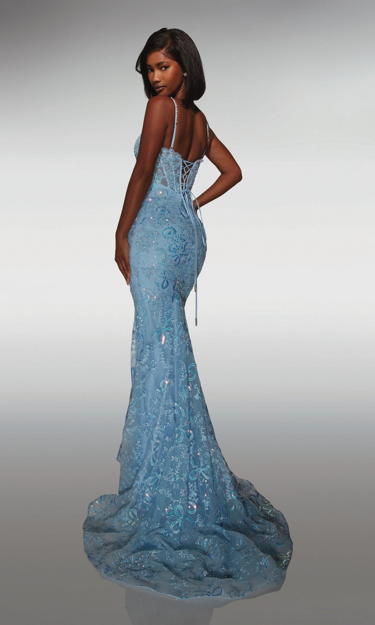 Woman wearing Alyce 62017—a long prom dress in light blue with a fitted silhouette, sequin accents, and lace-up back—stands and looks over her shoulder.